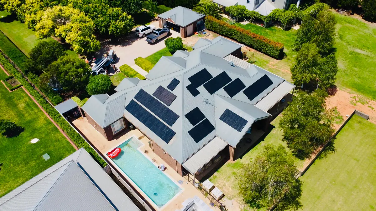 Drone view of a large home with a pool and solar panels on several faces of its grey metal roof