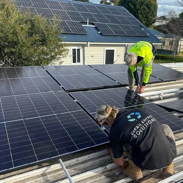 Two installers, one in a Clean Energy Solutions shirt, fixing solar panels to rails on a corrugated roof